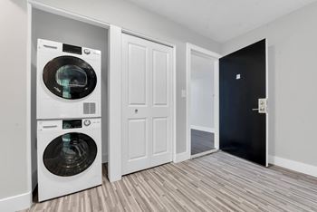 A white washing machine is in a small room with a black door.